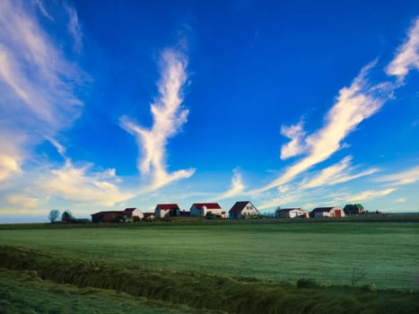 A green field with houses and clouds in the sky. Photo of a picturesque green field with houses and fluffy clouds in the sky in Iceland