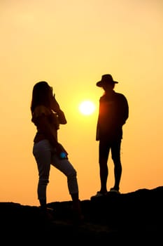 Women and men silhouettes on a rock at sunset.