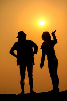 Women and men silhouettes on a rock at sunset.