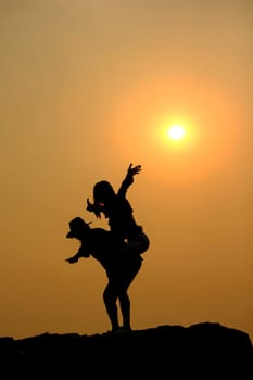 Women and men silhouettes on a rock at sunset.