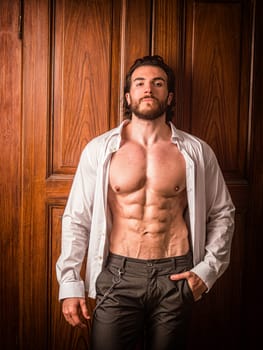Sexy handsome man standing in white open shirt with a smile in front of wood closet doors