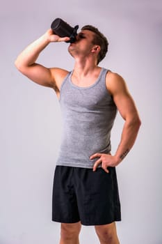 A man is drinking from a water bottle or a shaker containing a protein shake