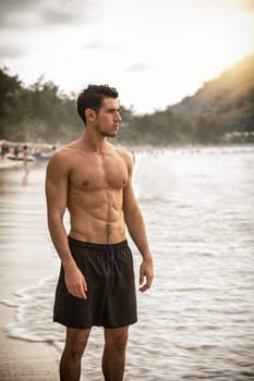 Attractive young man standing on a beach in Phuket Island, Thailand, shirtless wearing boxer shorts, showing muscular fit body