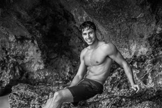 Half body shot of a handsome young man standing on a beach in Phuket Island, Thailand, shirtless wearing boxer shorts, showing muscular fit body, looking at camera