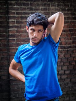 Three quarters shot of one handsome young man in urban setting wearing blue polo shirt in front of brick wall