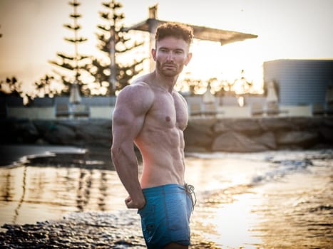 A shirtless muscular man walking into the ocean at dawn