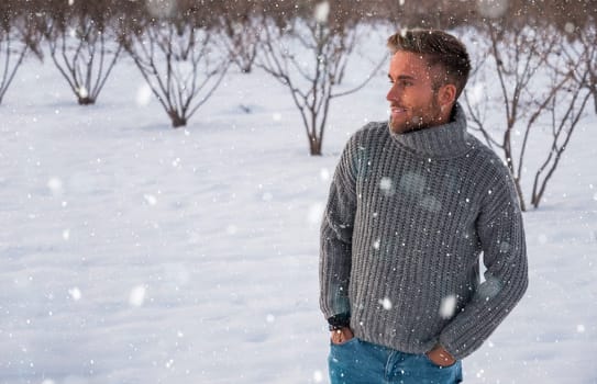 Portrait of young man posing outdoor in winter setting with snow all around, looking away to a side.