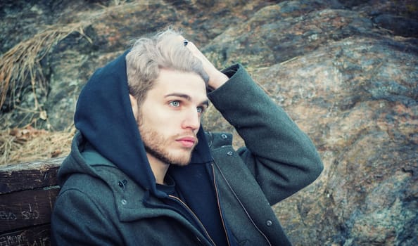 Portrait of young man in hoodie posing outdoor in winter setting with snow all around, looking away to a side.