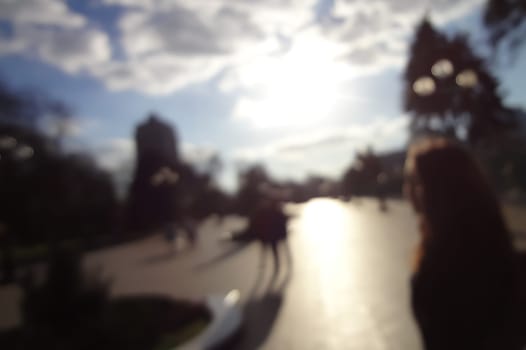 Blurred background of a city street and passing people. Sunny cool morning, cloudy sky. Backdrop