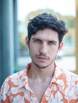 Head and shoulders shot of one handsome young man with green eyes in urban setting, looking at camera, wearing t-shirt