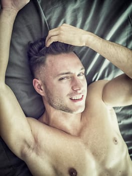 A shirtless man laying on top of a bed, smiling and looking at camera