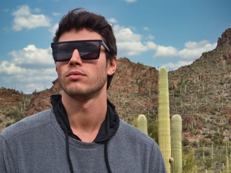 A man wearing a pair of sunglasses standing in front of a cactus in Saguaro National Park in Arizona, USA