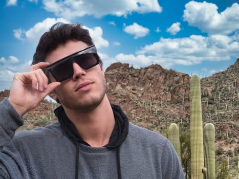 A man wearing a pair of sunglasses standing in front of a cactus in Saguaro National Park in Arizona, USA