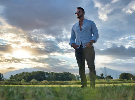 A man standing in a field with his hands in his pockets. Photo of a man standing in a field with his hands in his pockets