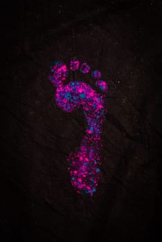 A pink and blue foot print on a black surface. Photo of a colorful footprint on a dark background