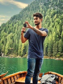 A man standing on a boat holding a camera. Photo of a man capturing the breathtaking beauty of the Dolomites from a boat in Italy