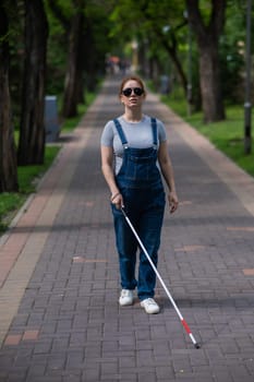 Blind pregnant woman walking in the park with a cane