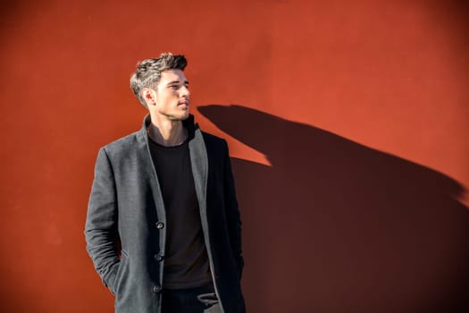 A man standing in front of a red wall, looking to a side