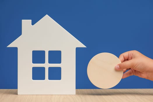 Real estate rental banner. White model of a house and a hand holding a sign mockup for an inscription as a symbol of rental housing. High quality photo. Copy space