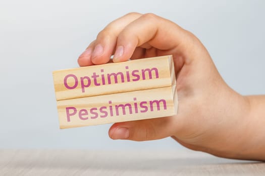 Optimism and pessimism. The hand holds 2 wooden rectangles next to each other with the inscriptions OPTIMISM AND PESIMISM. High quality photo