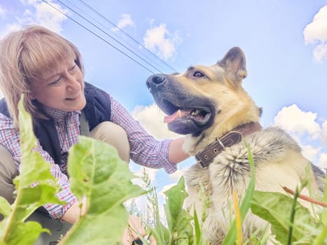 A girl or a woman and a German shepherd or Eastern European Shepherd dog in the forest, in nature, on spring, summer, or autumn day and blue sky. The concept of friendship between humans and animals