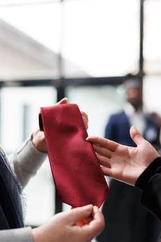 Elderly customer holding red tie analyzing material in clothing centre, shopping for formal clothes and elegant accessories. Store employee helping woman to choose merchandise. Fashion concept