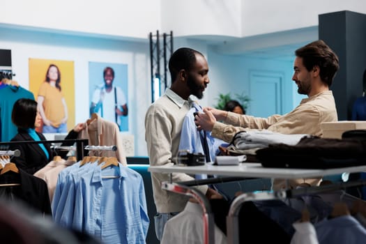 Clothing store man assistant helping client to check shirt fit and size. Shopping mall boutique consultant giving fashion advice to customer, examining formal apparel and tie match