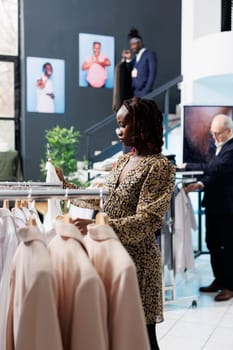 Pregnant woman looking at white shirt in modern boutique, shopping for fashionable maternity clothes. African american customer buying stylish casual wear in clothing store. Fashion concept