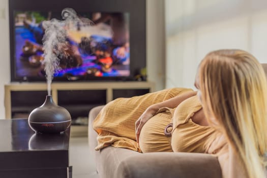 A blissful pregnant woman immerses in relaxation, savoring the soothing aroma from a diffuser while indulging in a calming TV video, embracing tranquility during her pregnant journey.