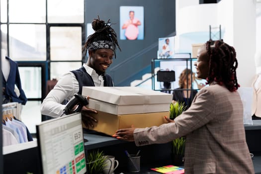 African american shopper holding packages fiiled with fashionable clothes, paying for merchandise at cash register in showroom. Customer buying stylish fashion collection, commercial activity