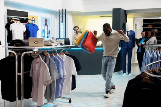 Excited african american shopaholic carrying shopping bags and dancing in clothing store. Fashion boutique happy cheerful client holding packages with apparel and having fun