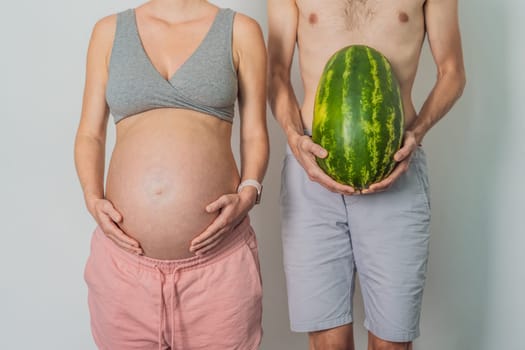 A humorous image: a pregnant woman and her husband playfully use a watermelon in place of a belly, comically highlighting the challenges of navigating with a pregnant bump.