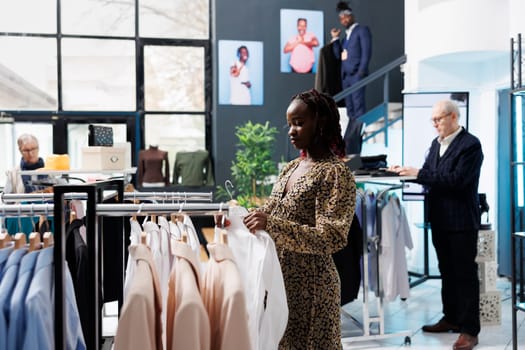 African american client looking at shirt for formal wear, checking fabric in clothing store. Stylish pregnant woman looking at new fashion collection, buying trendy merchandise and accessories