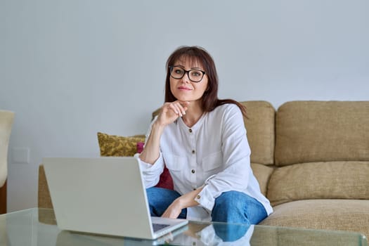 Middle aged business woman working at desk in home office, looking at camera with laptop computer. Work, remote business, job, online teaching, financial legal control, mature people lifestyle concept