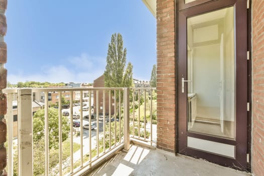 a balcony with an open door and cars parked on the street in the distance behind it is a red brick wall