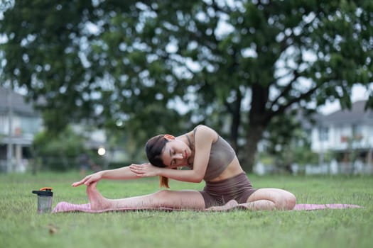 Young healthy Asian woman stretch her body on a yoga mat. Do yoga in a lush park Yoga and Pilates concept.