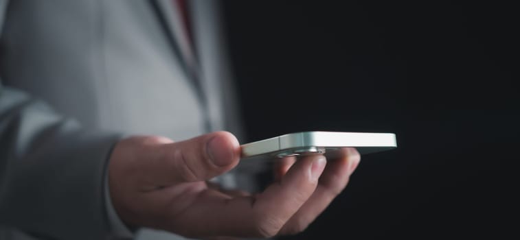 Close-up shot of businessman holding smartphone on dark background Represents business communication concepts.