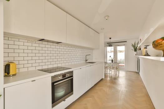 a modern kitchen with white cabinets and wood flooring in the middle of the room, there is an oven on the wall