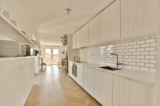 a kitchen with white cabinets and wood flooring in the center of the image is an open door leading to another room