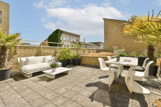 a patio with white furniture and plants on the side, in front of a brick wall that has been painted yellow