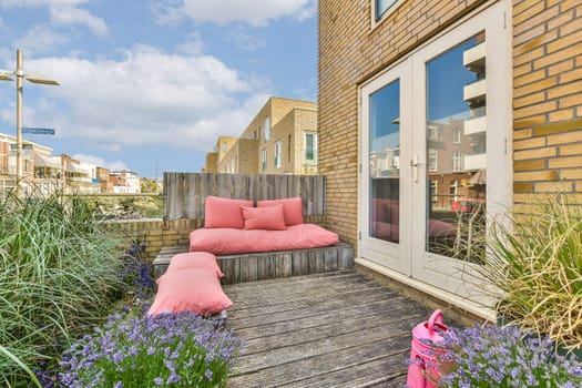 an outside area with some plants and flowers on the deck, including pink pillows and purple flowers in the fore