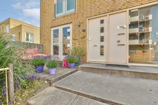 an outside area with flowers and plants on the steps in front of a brick building that has been painted white