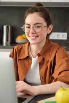 Vertical shot of woman working from home, business owner using laptop, browsing social media on computer, wearing glasses.