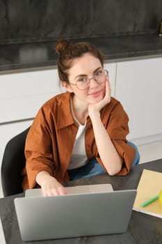 Vertical shot of woman working from home, business owner using laptop, browsing social media on computer, wearing glasses.