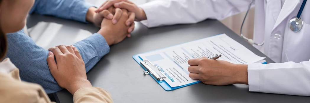 Doctor providing compassionate healthcare consultation while young couple patient holding hand, comfort each other after infertile report. Reproductive and medical fertility consulting. Neoteric