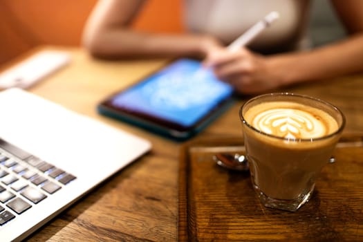 Freelance work in coffee shop. Focus on cafe latte. Female designer working in defocused background for copy space. Technology and digital art concepts.