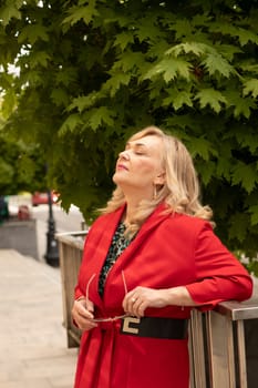 Portrait Relaxed Attractive Business Lady, Mature Sexagenarian Woman with Closed Eyes Outdoor. Stylish Senior Female in her 60s Holds Sunglasses. Boss or Manager Meditates. Vertical Plane.