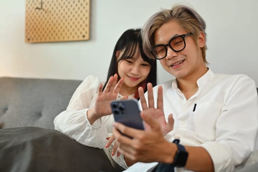 Happy asian couple making video call with a mobile phone with friends while relaxing at home.