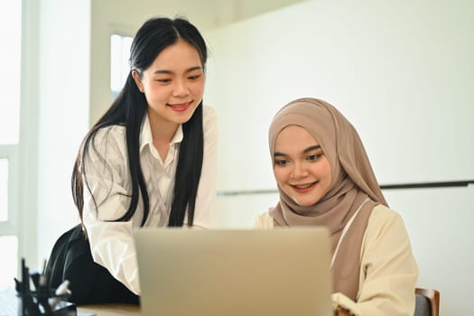 Smiling female colleagues using laptop and working on project modern in office.