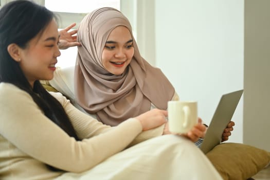 Happy young Muslim woman watching video or surfing internet laptop with her best friend.